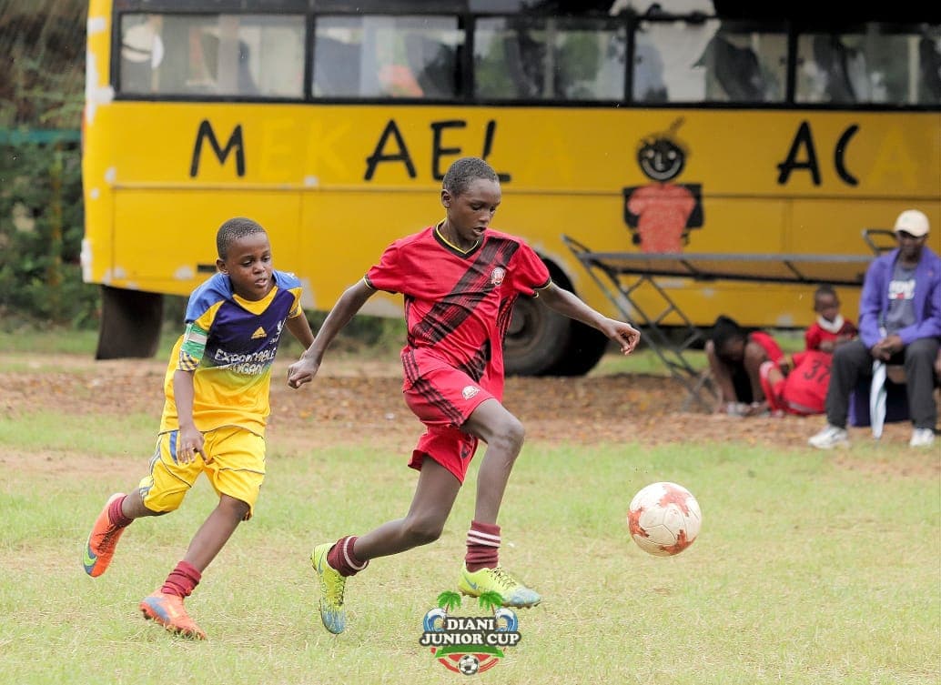 Two DJC footballers chasing possession in an opening-stage match.