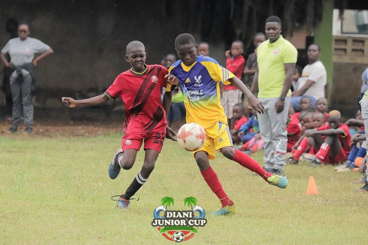 A red-shirted youth player driving forward under pressure at DJC.