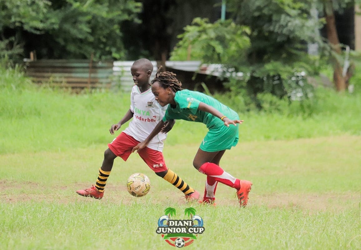 Two young players competing for the football at Diani Junior Cup.